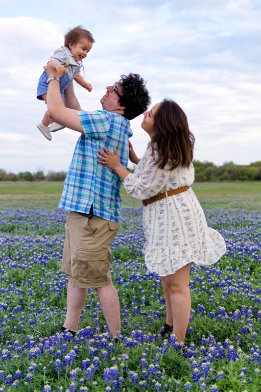 Nick lifting their son Ben in a Texas bluebonnet field with Andie smiling, 2024